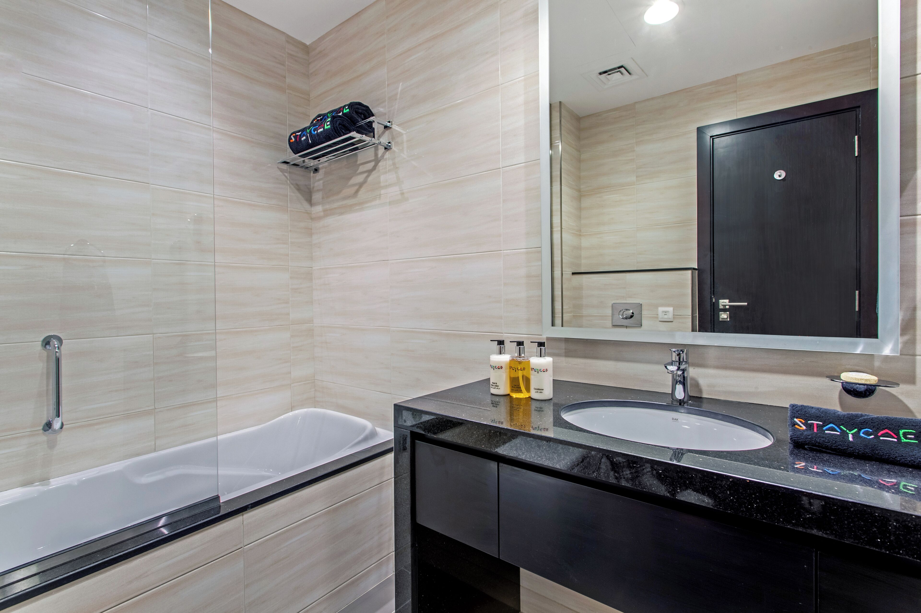 A modern bathroom with a bathtub, a sink, and a mirror. There are toiletries on the sink counter.