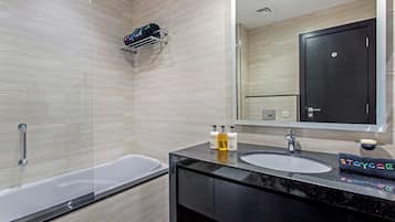 A modern bathroom with a bathtub, a sink, and a mirror. There are toiletries on the sink counter.