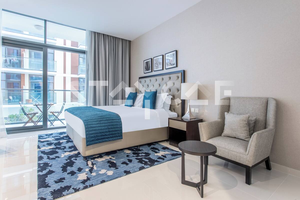 A modern hotel room with a large bed, a chair, a small table, and a view of the city through large windows.