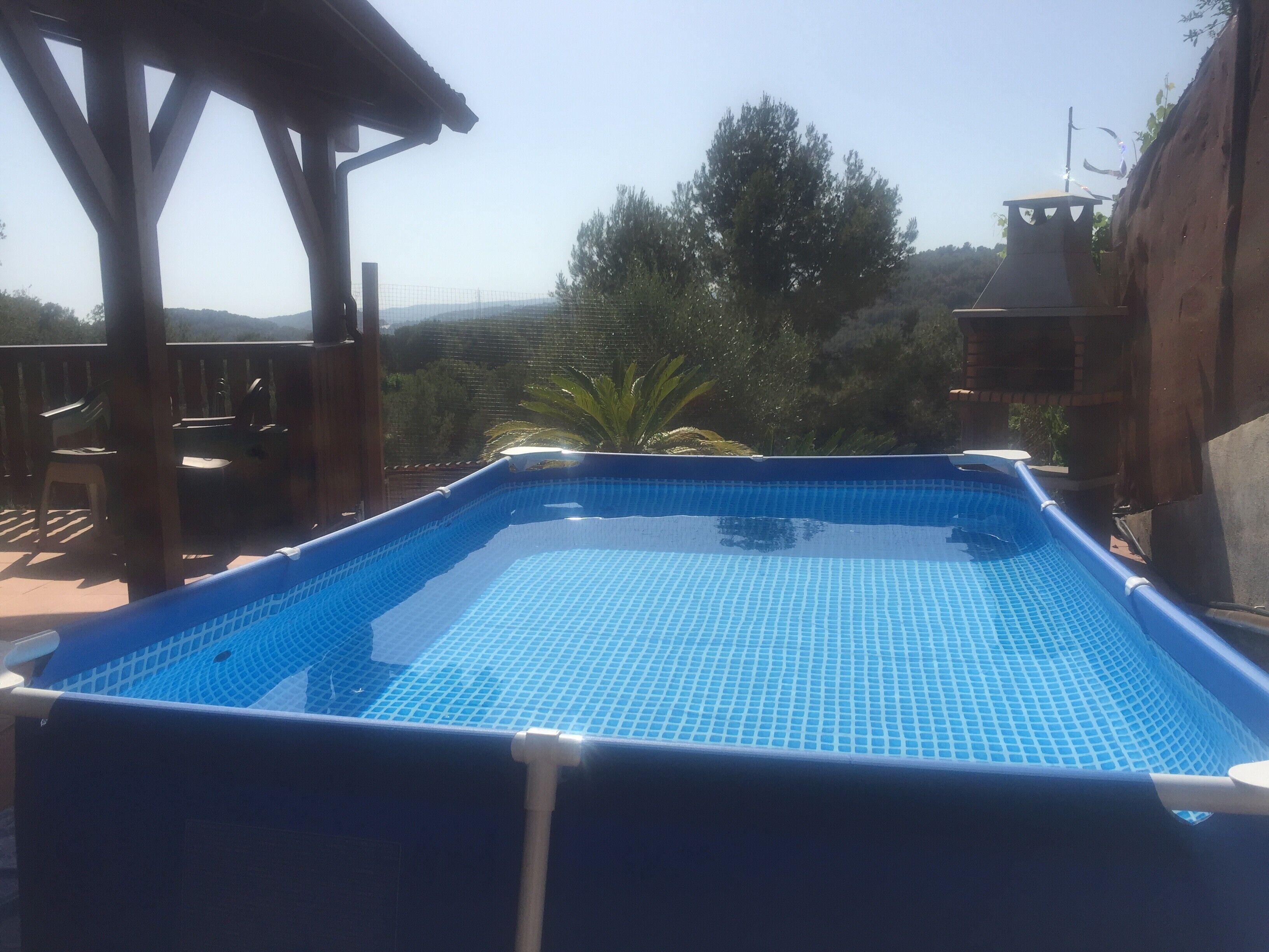 Una piscina exterior con terraza de madera y una pérgola.