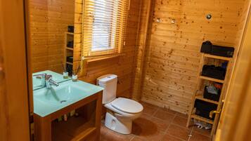 Een houten badkamer met een glazen wastafel, een wit toilet en een houten plank met opbergdozen.