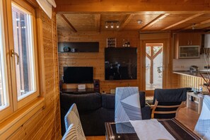 A wooden cabin interior with a living area, sofa, TV, and kitchen. - Chalet 'Casa de Madera' with Mountain View, Garden, A/C, Pool & Wi-Fi (Calafell)