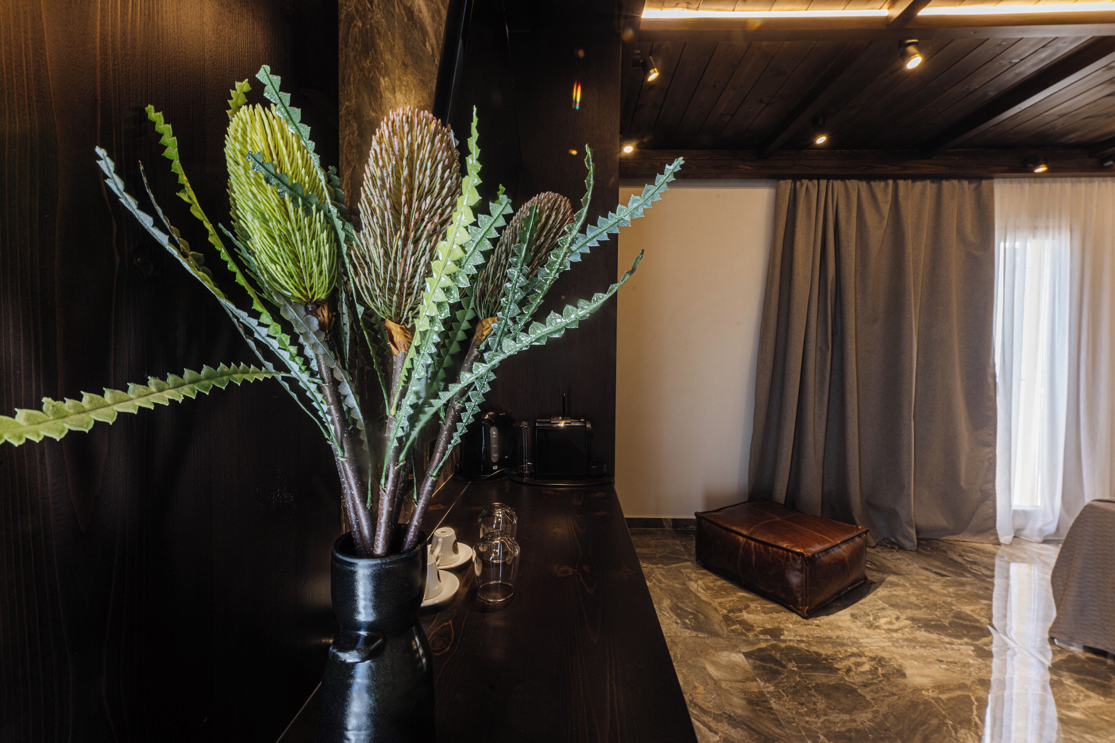 Un interior de madera oscura con un florero de plantas verdes, una cafetera y un reposapiés de cuero.