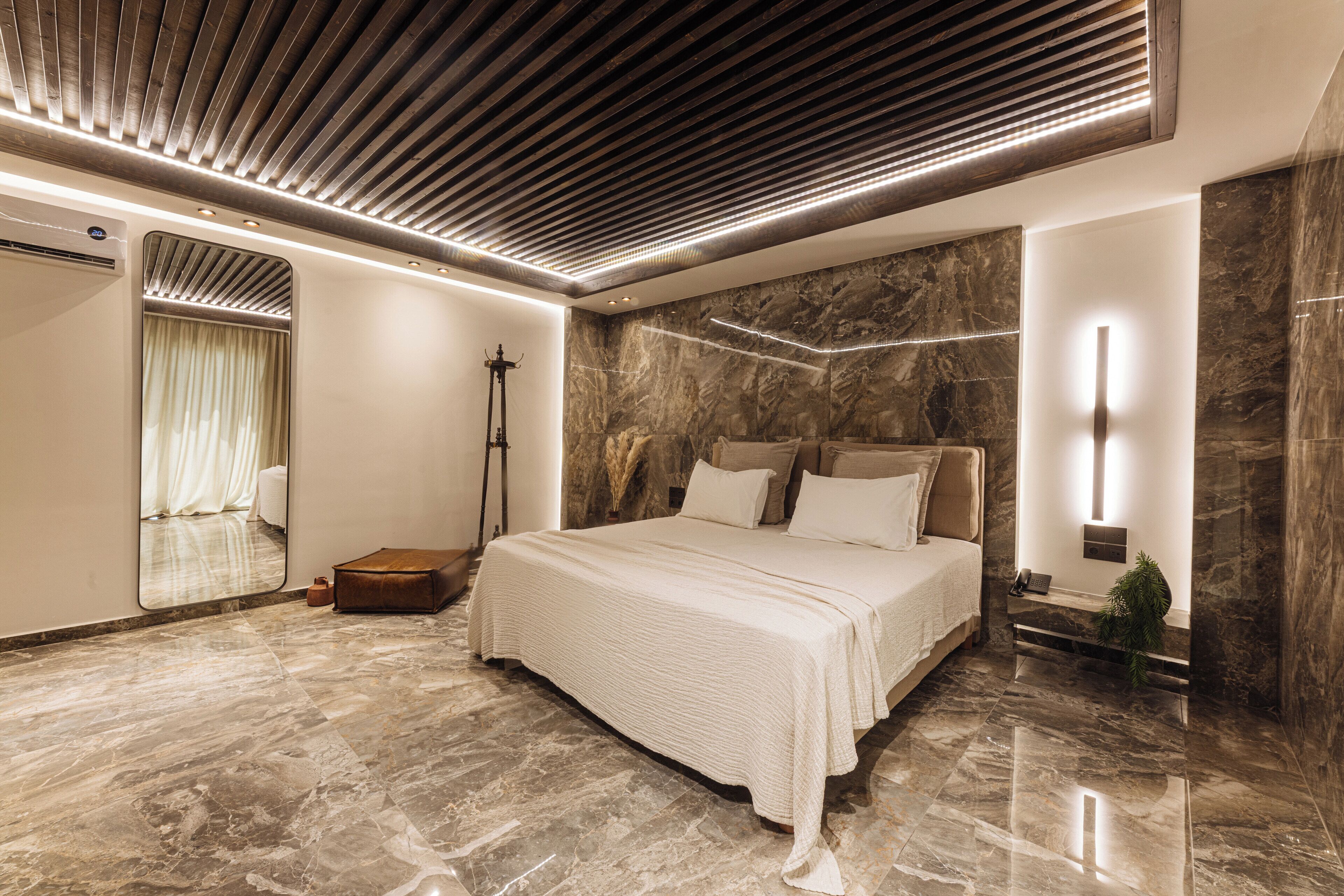 A modern bedroom with a large bed, a mirror, and a nightstand.