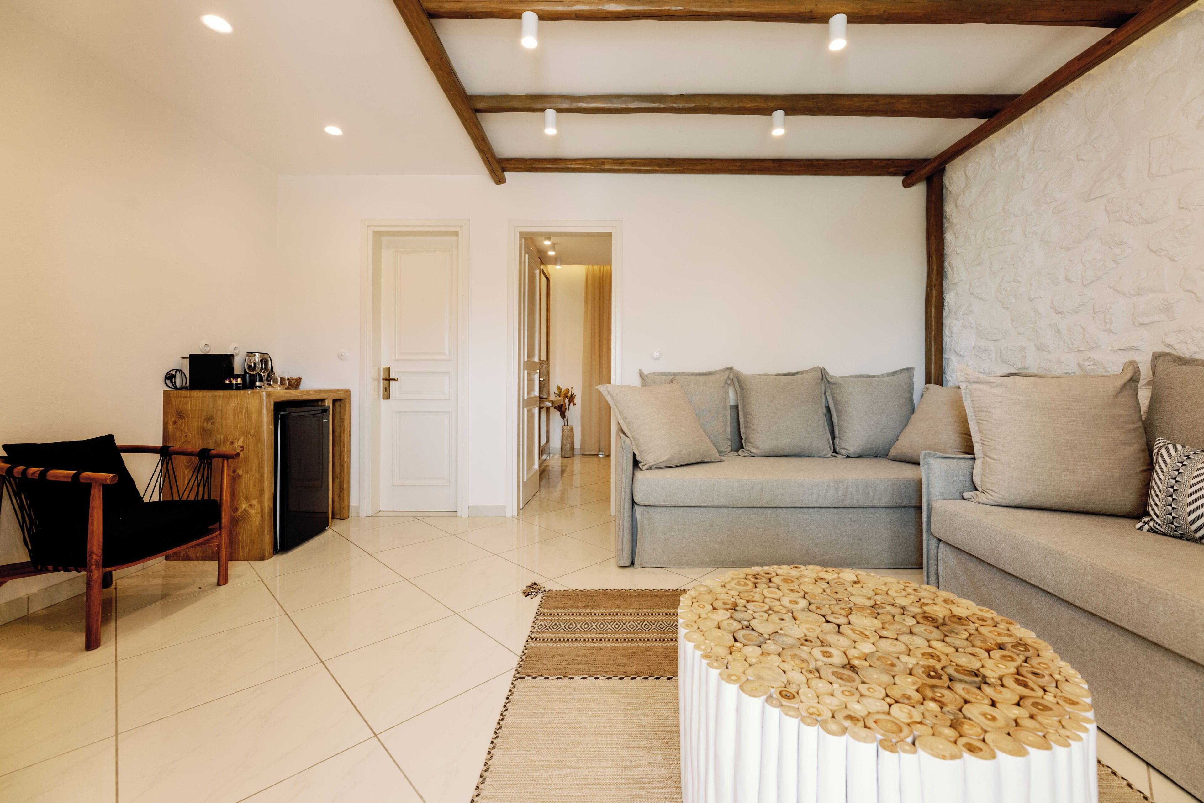 A living room with a sofa, a coffee table, a wooden bench, and a small kitchen area with a refrigerator.