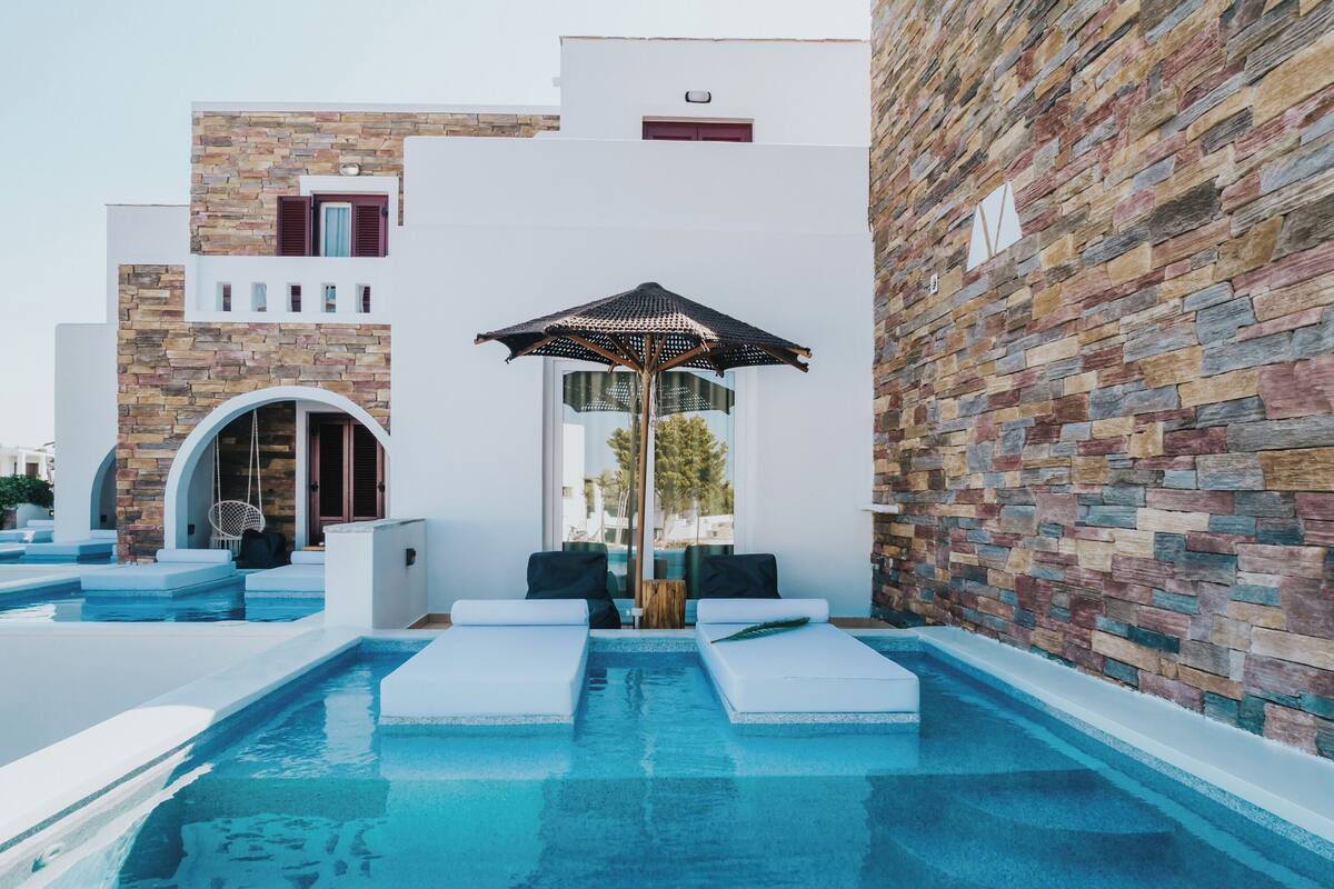 A modern pool area with a stone wall, a hanging chair, and a lounge chair.