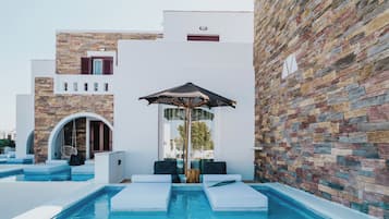 Un área de piscina moderna con un muro de piedra, una silla colgante y una tumbona.