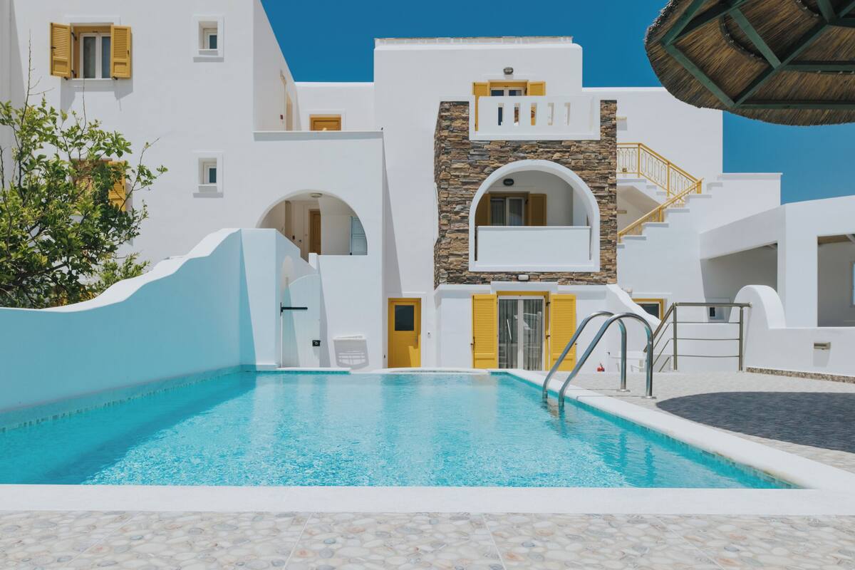 A swimming pool area with white buildings, stone accents, and yellow doors.
