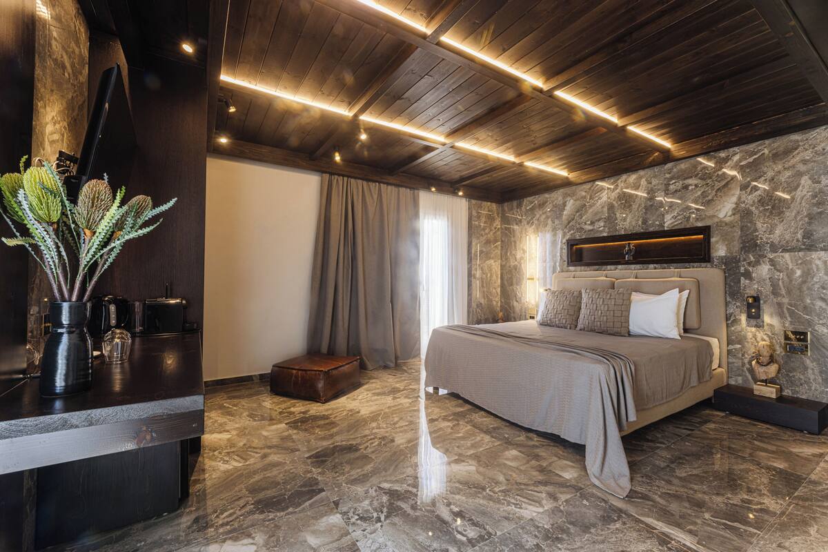 A modern bedroom with a large bed, stone walls, and a wooden ceiling.