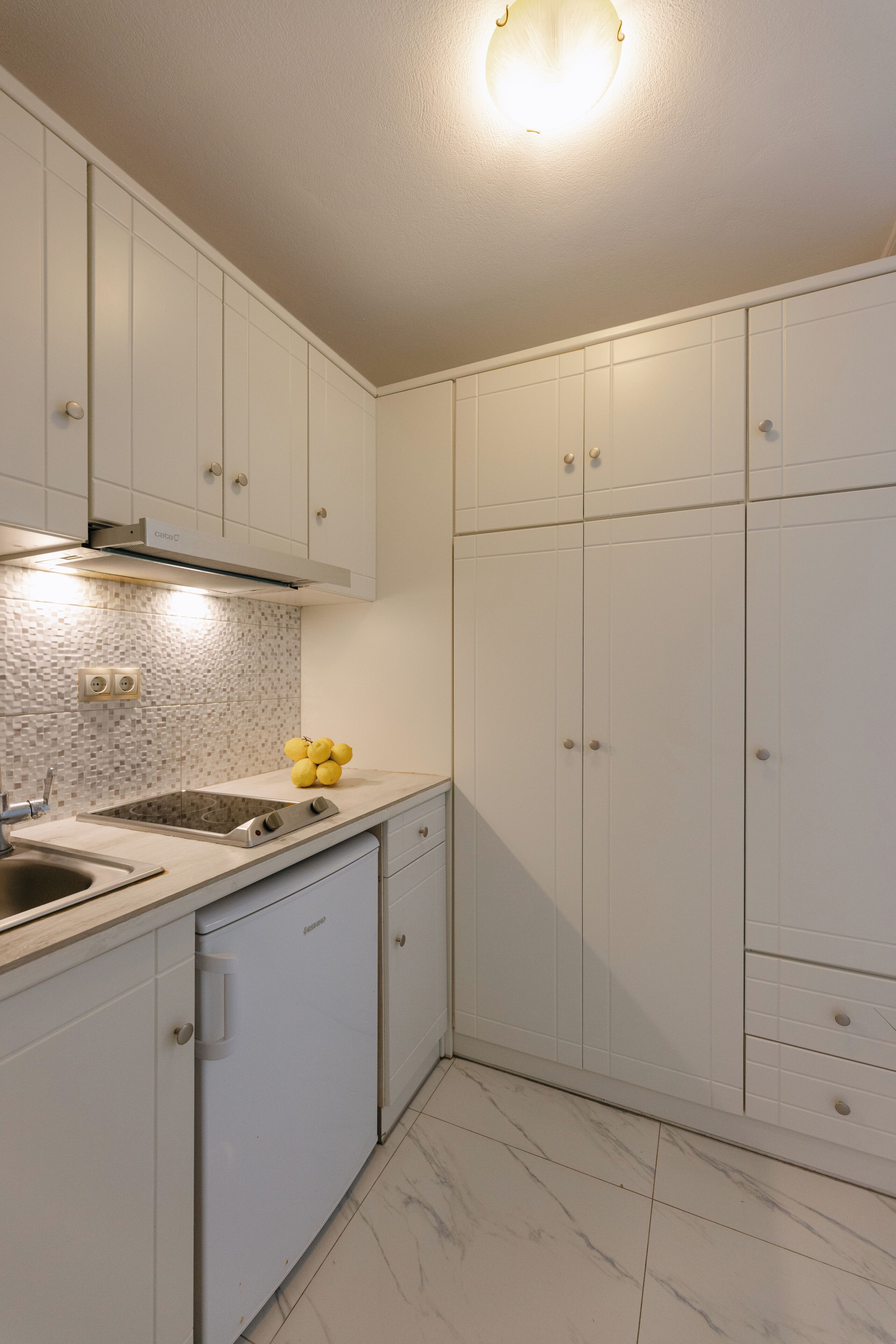 A modern kitchen with white cabinets, a built-in dishwasher, and a tiled backsplash.