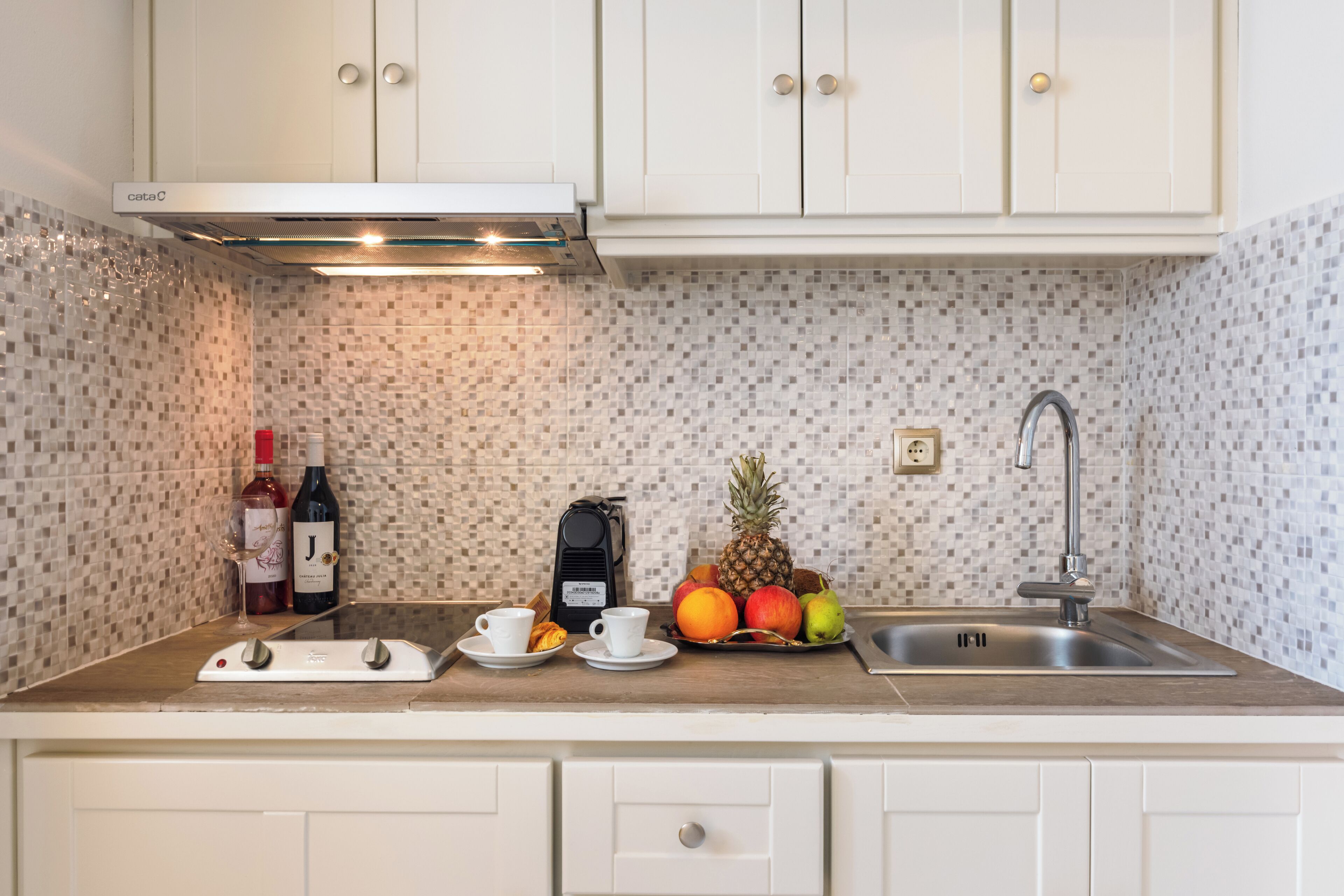 A kitchen with white cabinets, a tiled backsplash, a stainless steel sink, and a coffee maker.