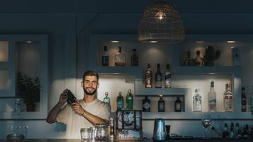 Un espace bar avec des étagères remplies de bouteilles d’alcool, un luminaire suspendu et un comptoir orné de verres et d’un cadre photo.