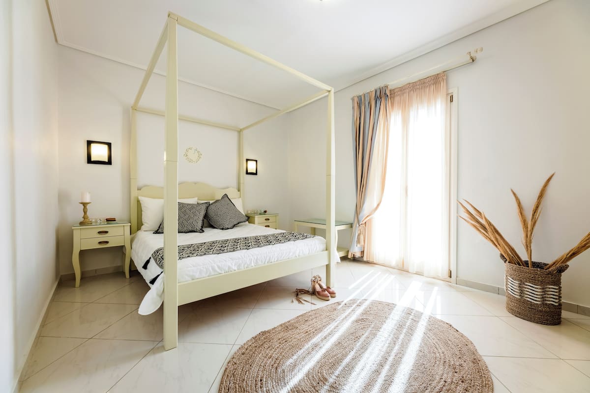 A bedroom with a four-poster bed, two bedside tables, a nightstand, a large woven rug, and a decorative basket with tall grasses.