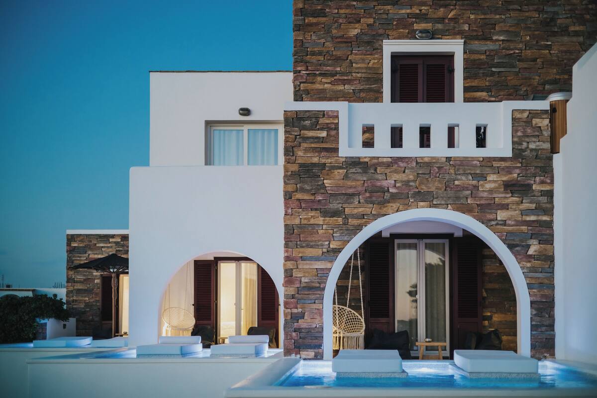 A modern building with stone and white facades, outdoor seating, and a pool area.