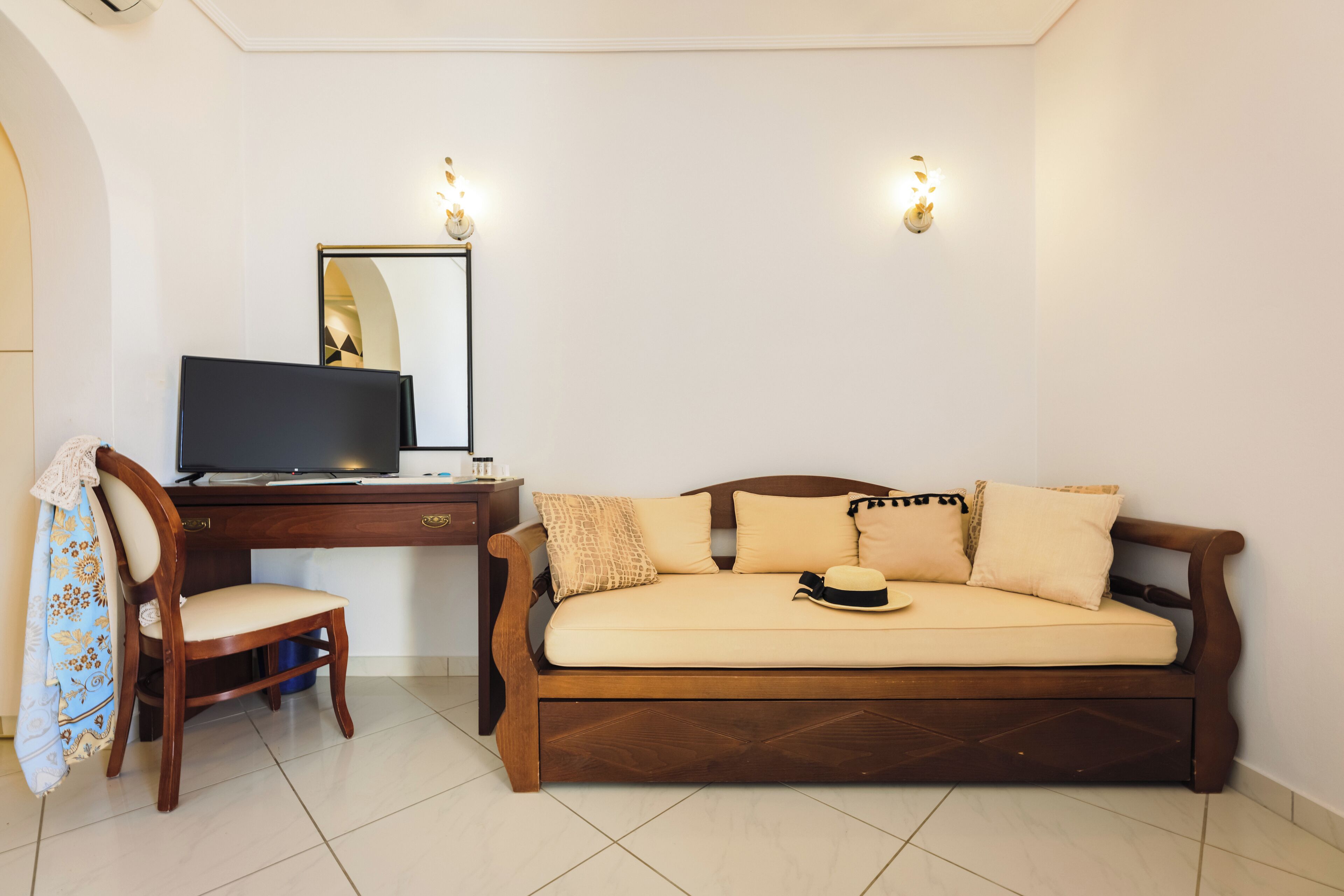 A room with a wooden desk, a television, a sofa, and two wall-mounted lights.