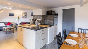 A modern kitchen with a central island, built-in appliances, and a dining area with a table set for two. - Seaside house with beach access, modern amenities and family space (Gatteville-le-Phare)
