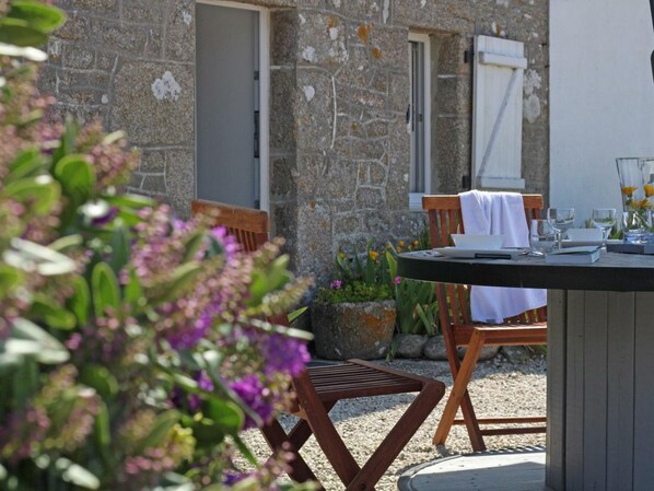 An outdoor dining area with a stone wall, wooden chairs, and a table set for two. - Seaside house with beach access, modern amenities and family space (Gatteville-le-Phare)