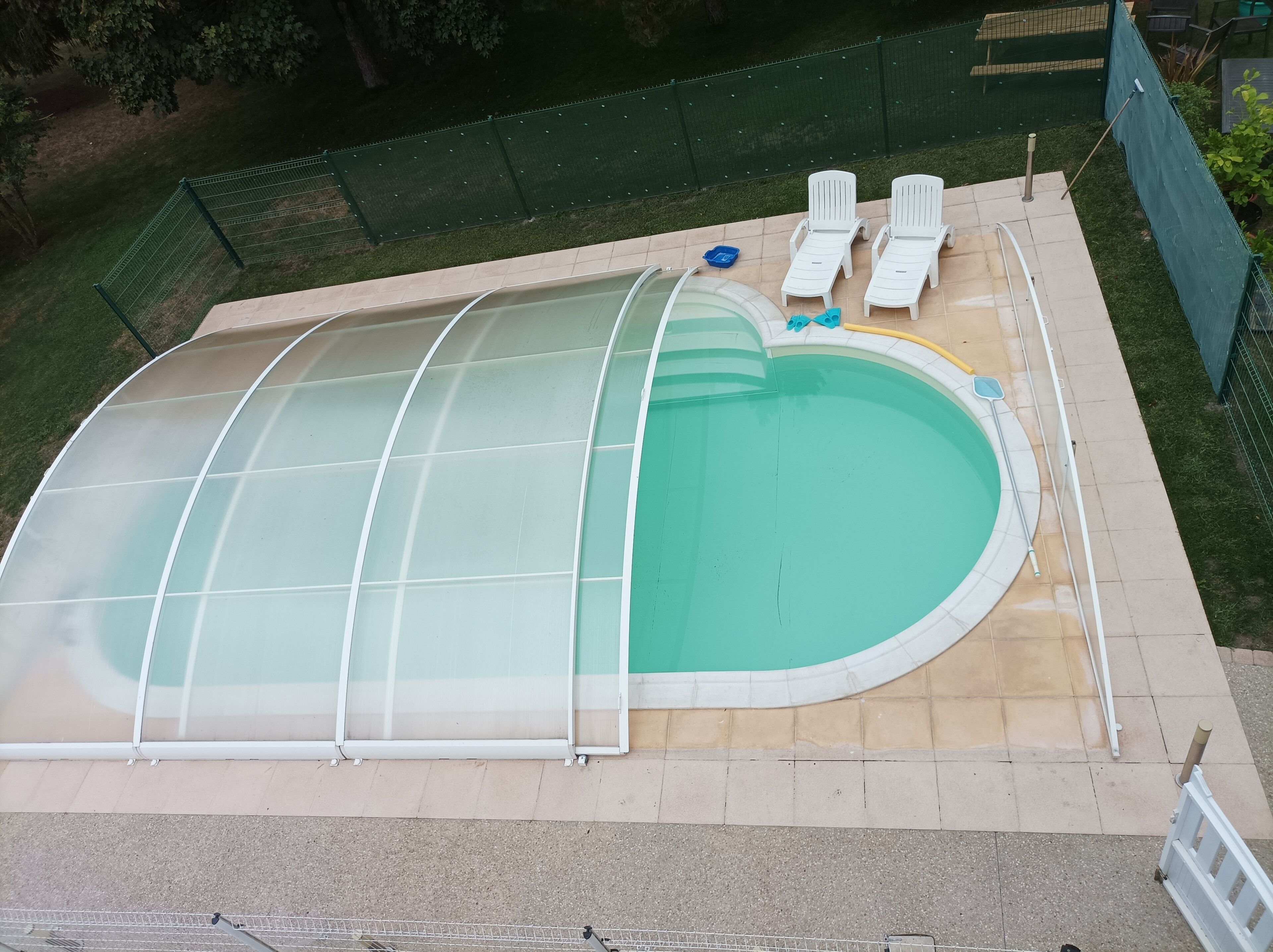 Una piscina techada con cerramiento de vidrio, dos sillas de descanso y una manguera.