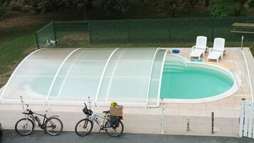 A swimming pool with a cover, surrounded by a fence, and a few bicycles parked nearby.