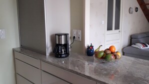 A kitchen with a coffee maker, fruit bowl, and a white cabinet.
