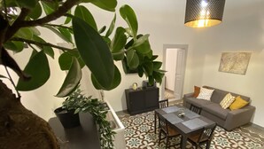 Ein Wohnzimmer mit einem gemusterten Boden, einer Couch mit Kissen, einem Esstisch mit Stühlen und einer Pendelleuchte.