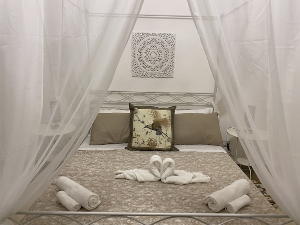 A bed with a canopy, a decorative pillow, and rolled towels arranged on the bed.