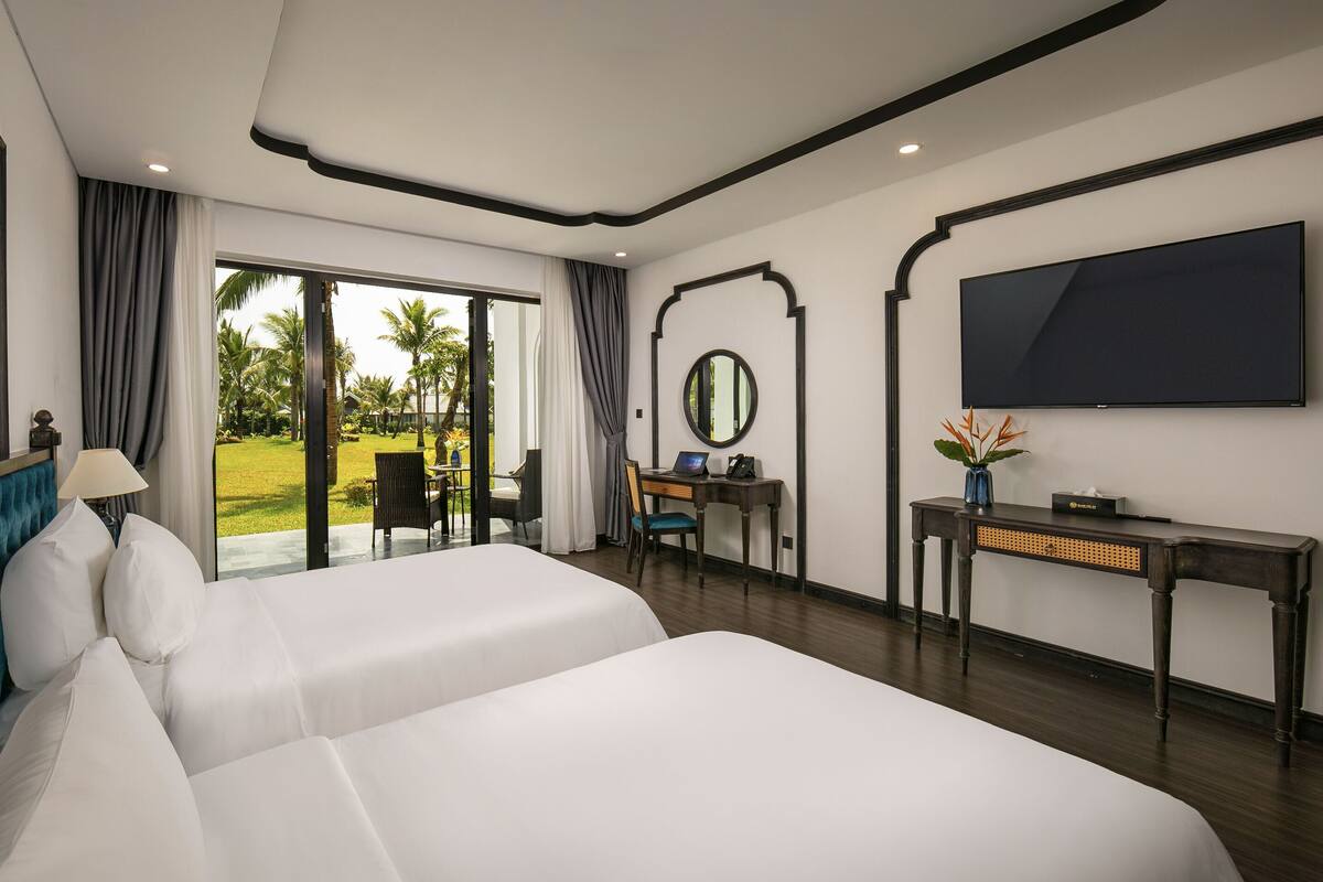 Une chambre d’hôtel avec deux lits, un bureau avec un ordinateur portable, une télévision et une vue sur un jardin.