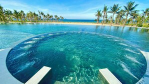 Une piscine à débordement circulaire, à l’eau d’un bleu cristallin, entourée d’une plage de sable et de palmiers, et offrant une vue imprenable sur l’océan.