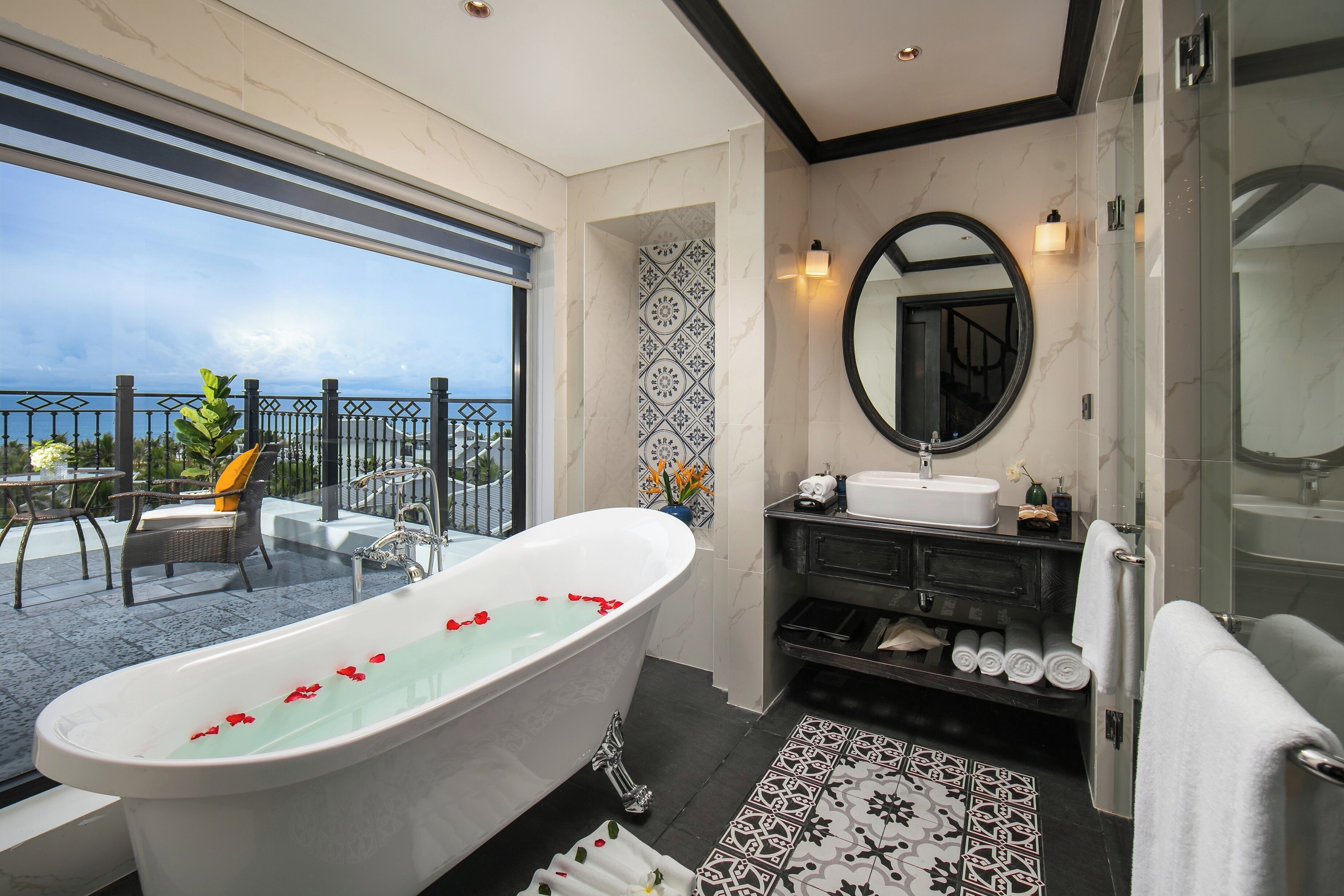 A modern bathroom with a freestanding bathtub, a large mirror, and a view of the sea.