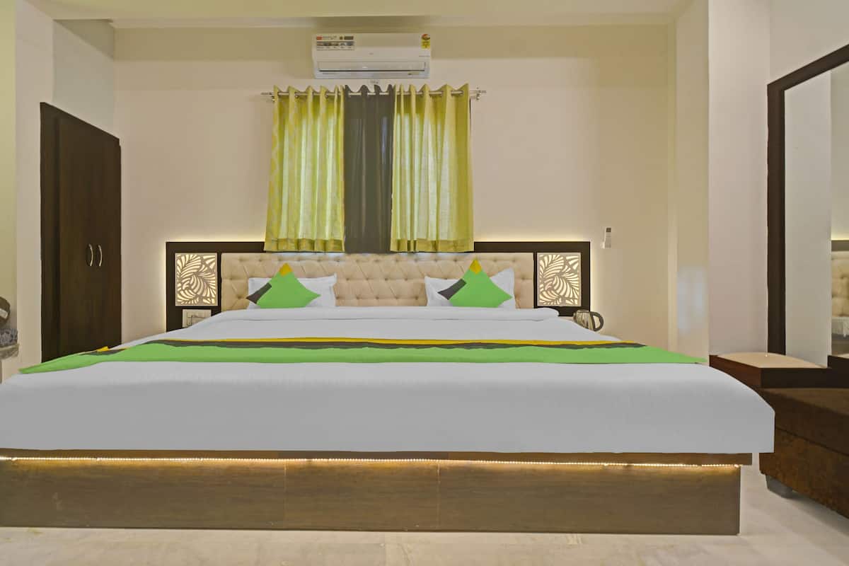 A hotel room with a large bed, a headboard with decorative panels, an air conditioning unit, and a window with curtains.