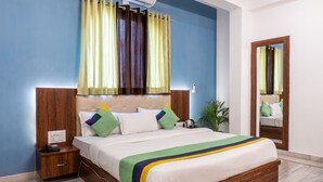 A neatly made bed with a wooden headboard, a bedside table with a phone, and a mirror on the wall. - Treebo The Fresco Lake Pichola (Udaipur)
