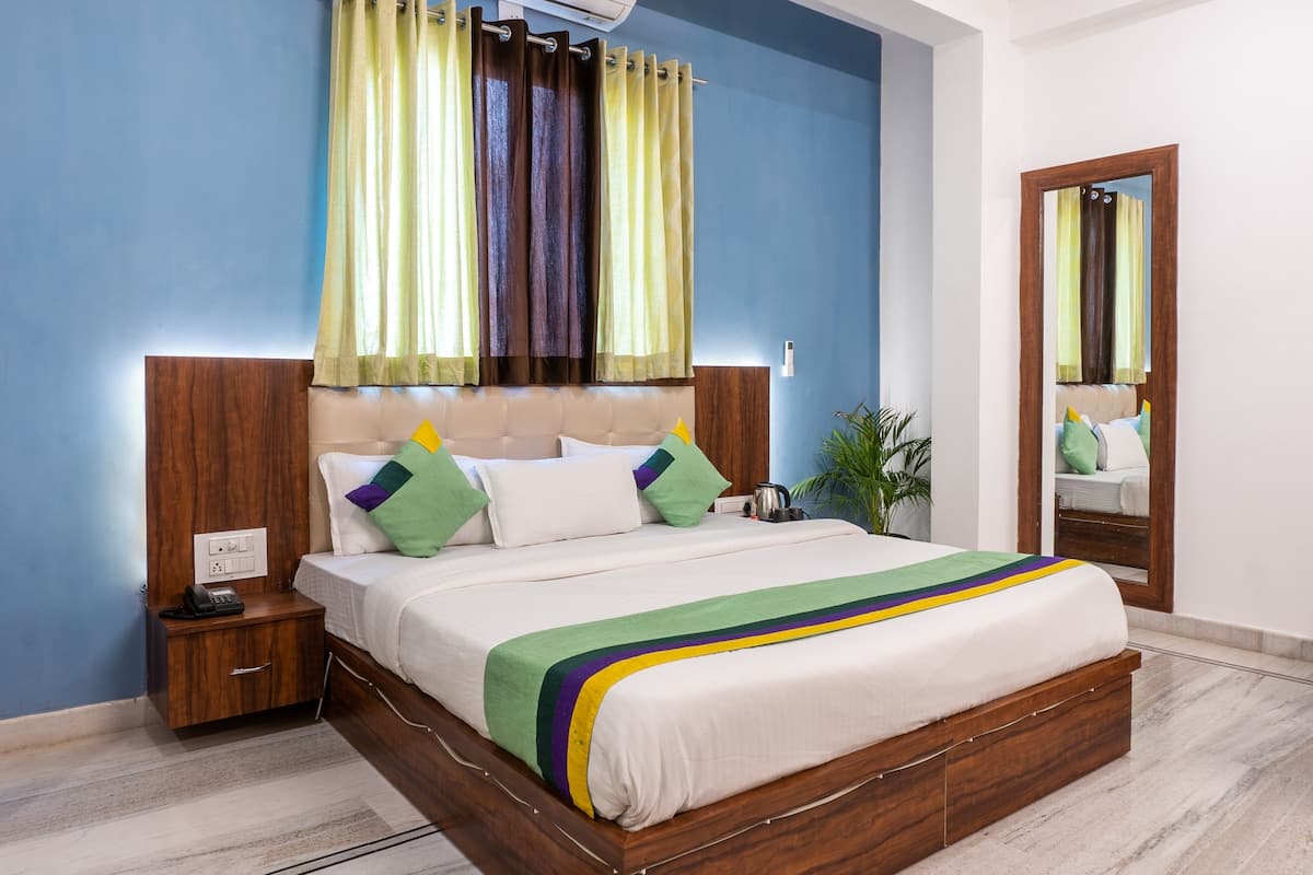 A neatly made bed with a wooden headboard, a bedside table with a phone, and a mirror on the wall.