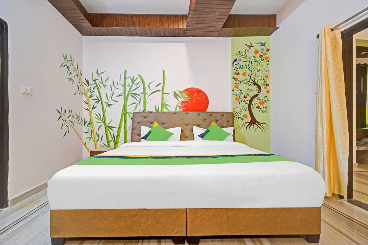 A bed with a wooden headboard, a green and yellow bedspread, and a wall mural with bamboo and a tree.