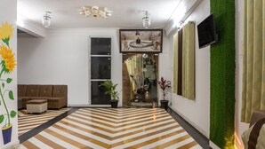 A modern living room with a chevron-patterned floor, a brown sofa, and a flat-screen TV mounted on a green wall. - Treebo The Fresco Lake Pichola (Udaipur)
