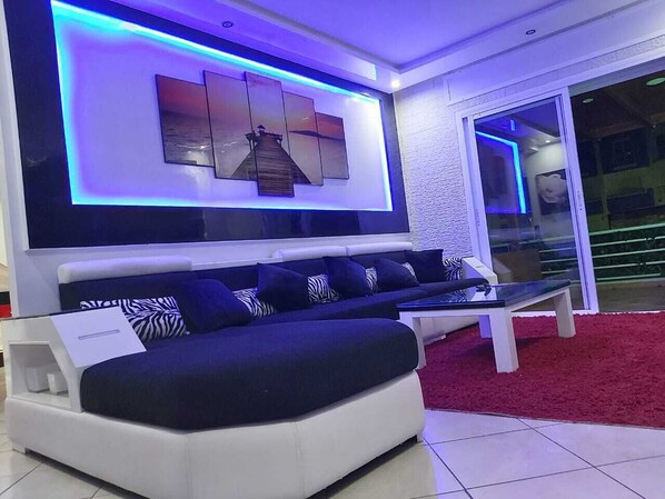 A modern living room with a sectional sofa, a flat-screen TV mounted on the wall, and a glass door leading to an outdoor area.