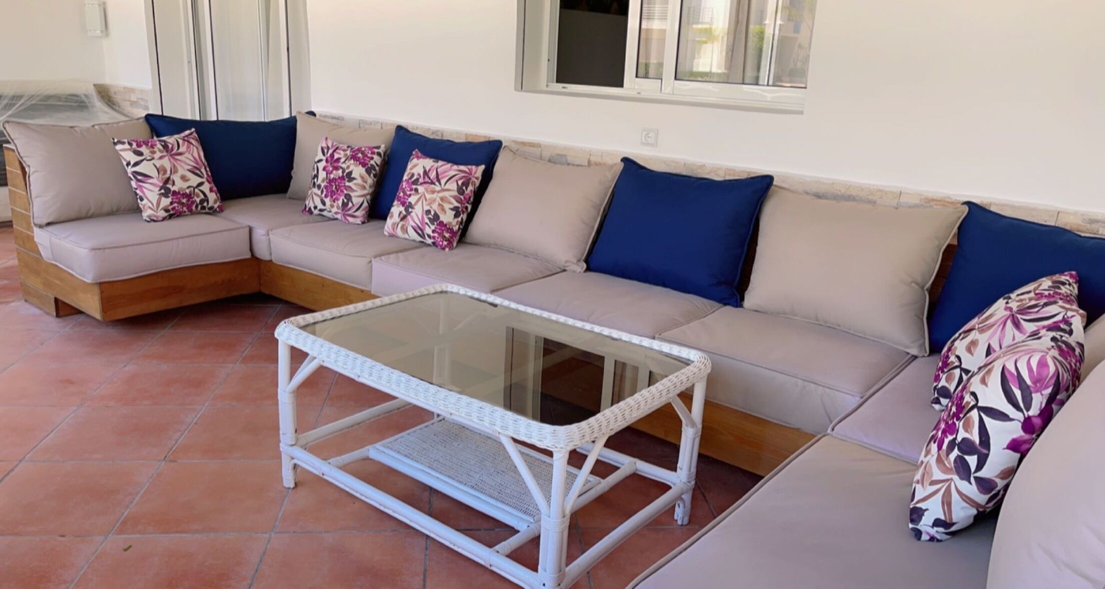 Un rincón amoblado con una mesa de centro de vidrio y un sofá con cojines estampados.