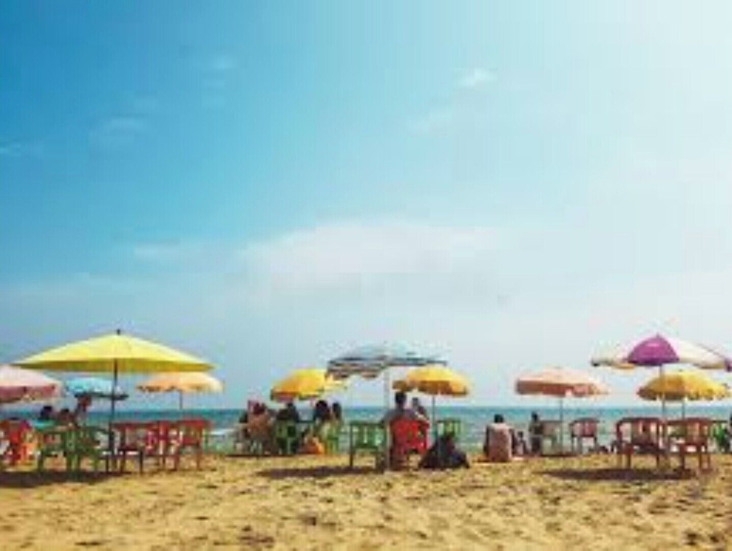 Een strand met rijen kleurrijke parasols en stoelen.