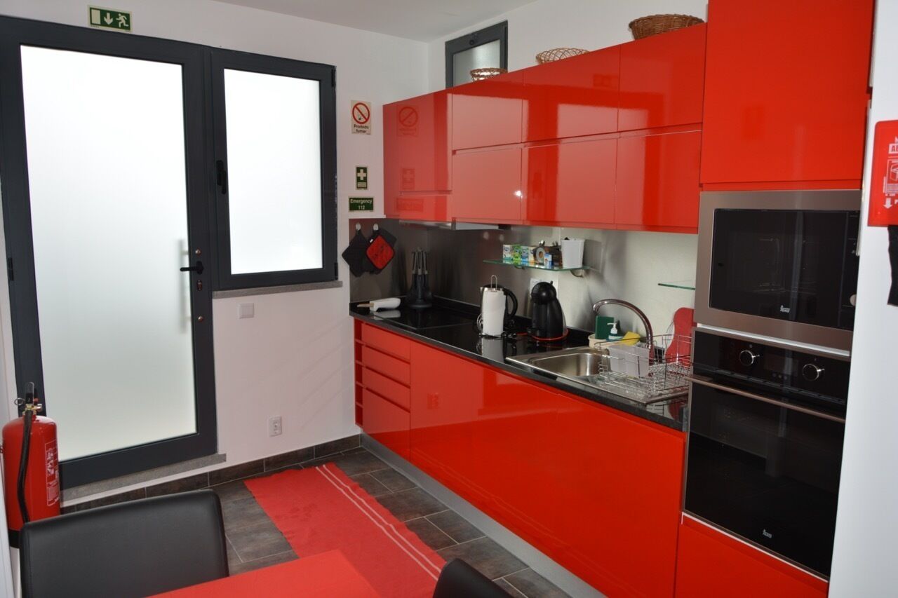 A modern kitchen with red cabinets, a stainless steel sink, and a black oven.