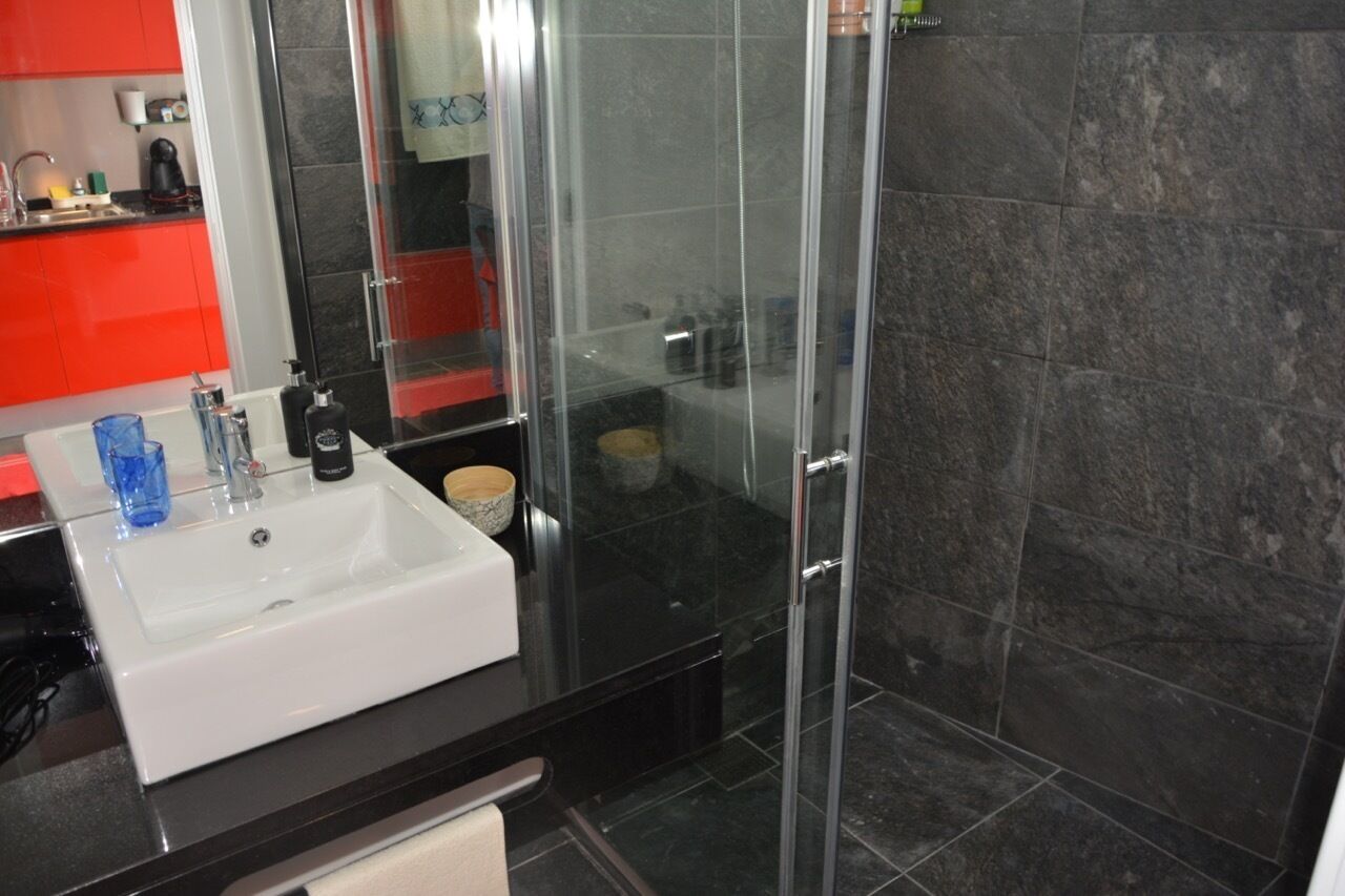 A modern bathroom with a white sink, black countertop, and a glass shower enclosure.
