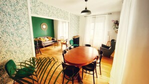 A dining area with a round wooden table surrounded by chairs, a green sofa, and a small side table. - Maison Chiche charming apartment 3 * 8 pers (Bain-de-Bretagne)