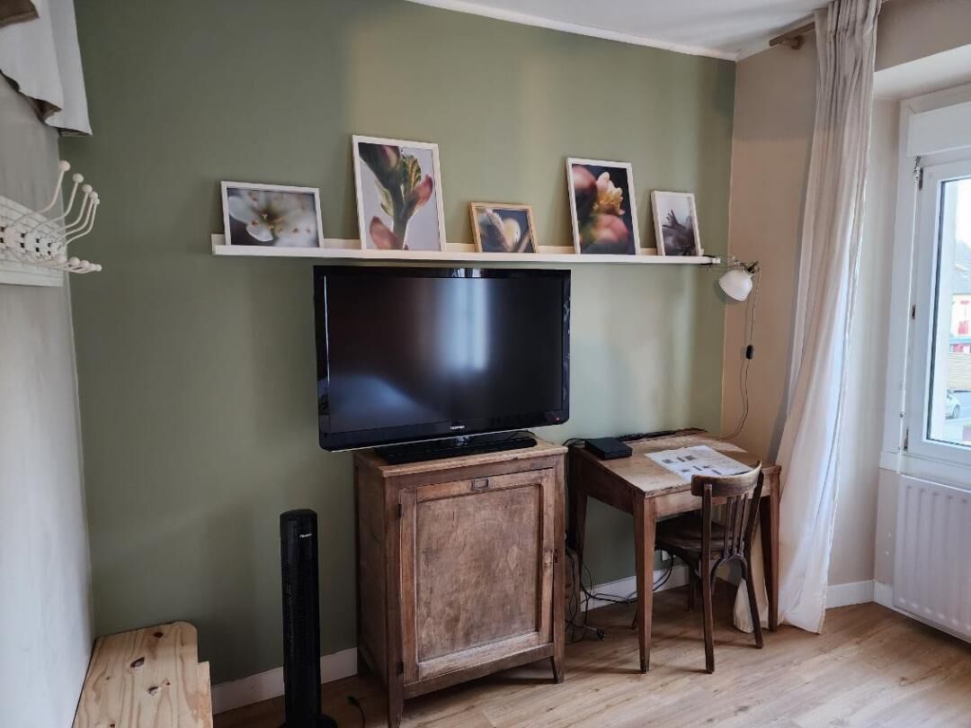 Un salon avec un téléviseur posé sur un meuble en bois, un bureau avec une chaise et une fenêtre avec des rideaux.