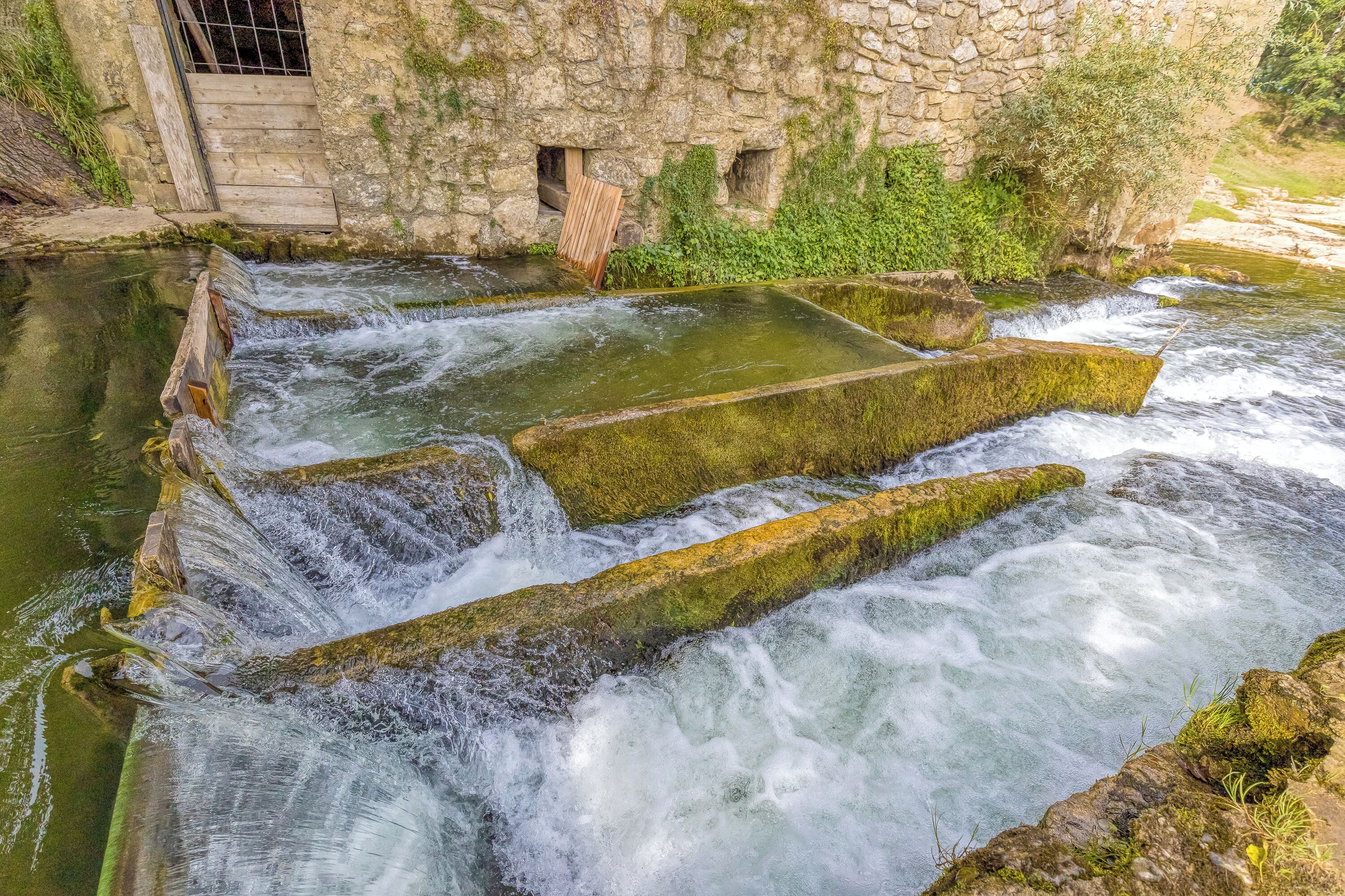 A stone structure with water flowing over it, surrounded by greenery.
