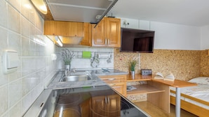 Uma cozinha compacta com armários de madeira, fogão embutido e uma pequena área de refeições com uma cama.