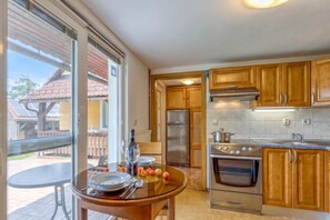 A kitchen with wooden cabinets, a stainless steel refrigerator, a stove, and a dining area with a glass table and chairs.