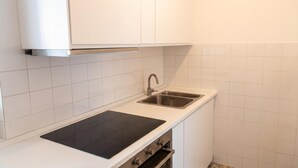 A kitchen with white cabinets, a black induction cooktop, a stainless steel sink, and a built-in oven. - Tre Balconi Sul Mare - Beachfront Sea-view Apartment (Borghetto Santo Spirito)