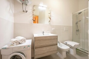 Une salle de bain moderne Ă©quipĂ©e dâun lave-linge, dâun Ă©vier, dâun bidet et dâune douche Ă parois de verre.