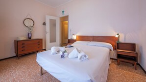 A hotel room with a bed, a dresser, a nightstand, a lamp, and a mirror on the wall. - Tre Balconi Sul Mare - Beachfront Sea-view Apartment (Borghetto Santo Spirito)