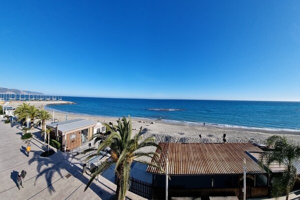 Un paseo marítimo frente a la playa con un restaurante, palmeras y vistas al océano.