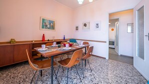 A dining area with a table set for four, chairs, a wooden cabinet, and a painting on the wall. - Tre Balconi Sul Mare - Beachfront Sea-view Apartment (Borghetto Santo Spirito)