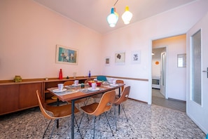 Un coin repas avec une table en bois, des chaises et un banc. Des tableaux encadrés ornent le mur, et une porte donne accÚs à une autre piÚce.